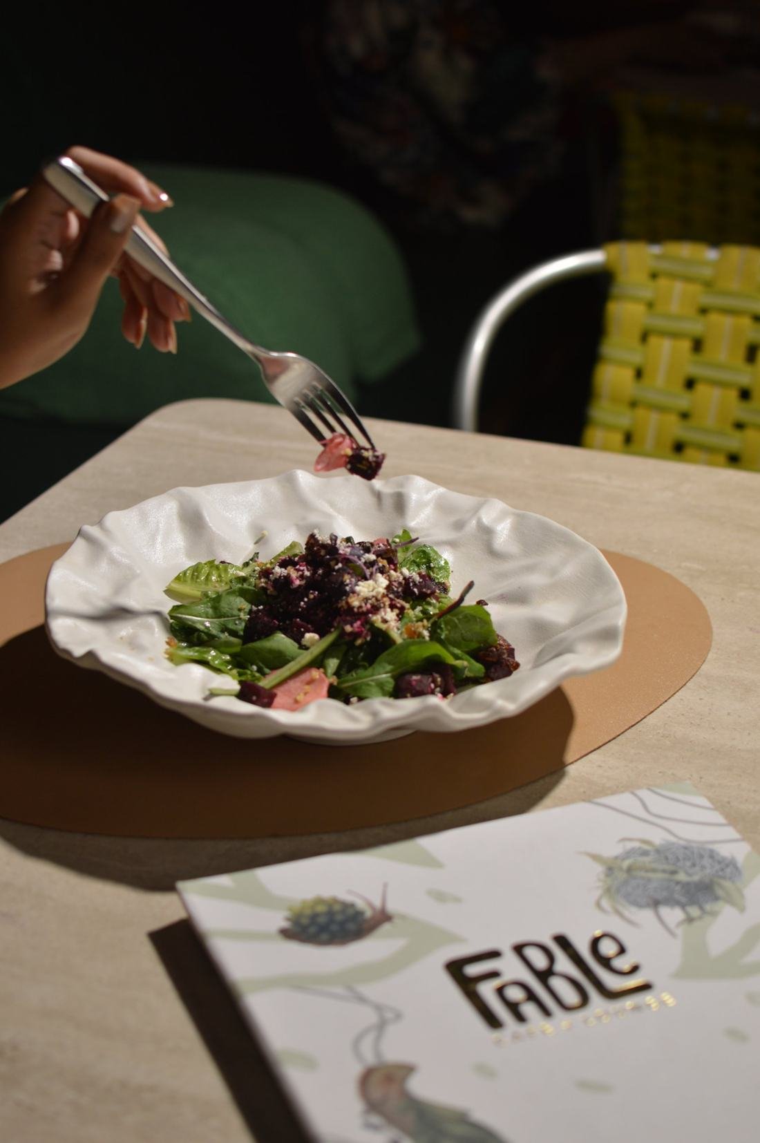 A beet and greens salad being eaten beside a Fable menu